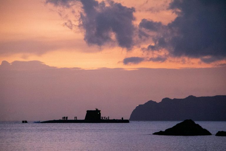 Silhouettes of People Standing on a Surfacing Submarine at Dusk