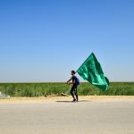 man in black jacket holding green umbrella walking on brown sand during daytime