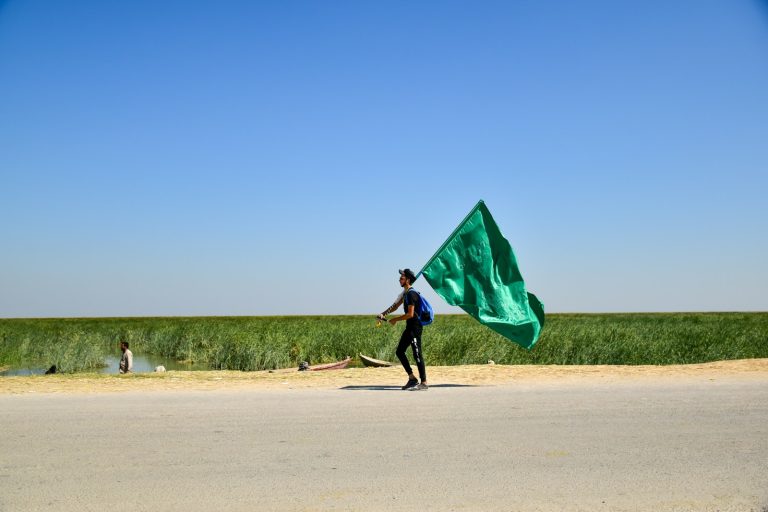 man in black jacket holding green umbrella walking on brown sand during daytime