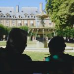 a couple of people sitting in front of a fountain in front of a large building