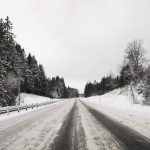 a snow covered road with trees and a fence