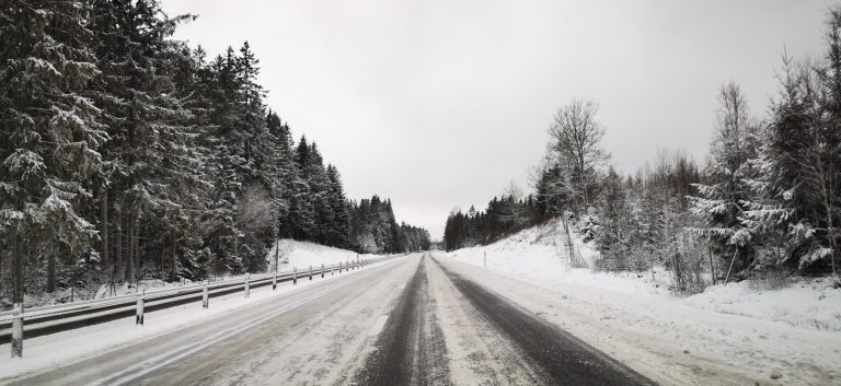 a snow covered road with trees and a fence