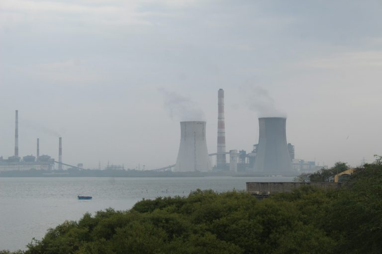 smoke stacks rise from a factory near a body of water