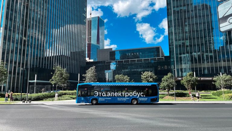 A blue bus driving down a street next to tall buildings