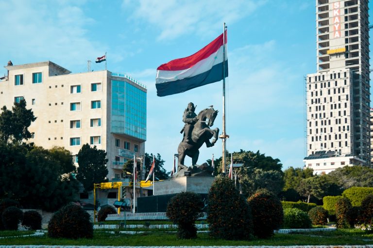 En statue av en mann som rir på hest og flagget av Syria